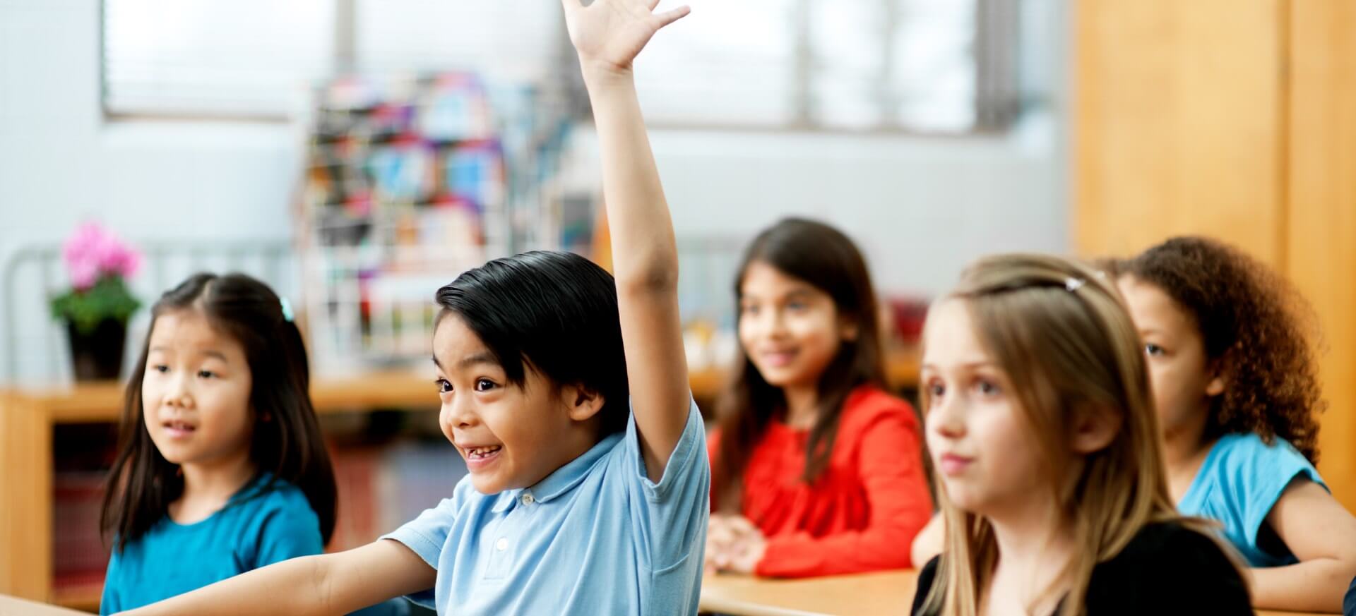 One student raising his hand inside the classroom with other students